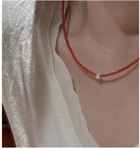 Detail of red agate beaded necklace with silver zircon charm on collarbone