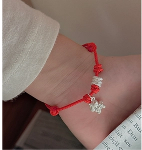 Detail of red braided S925 silver bracelet with small horse pendant on woman wrist