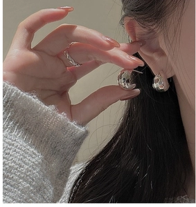 Macro detail of silver S925 earrings and wave ring with textured hammered finish on skin