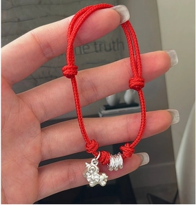 Detail of red braided cord bracelet featuring a S925 silver pig charm and silver beads