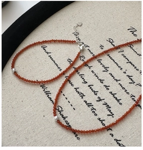 Detail of S925 silver necklace with faceted reddish beads and heart charm on linen