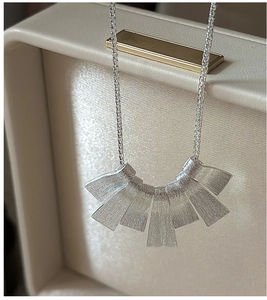 Close-up of S925 sterling silver necklace with brushed trapezoid pendants on leather box