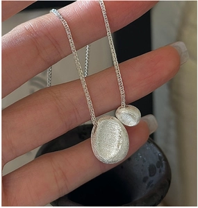 Close-up of S925 silver necklace featuring two brushed irregular pebble pendants on a chain