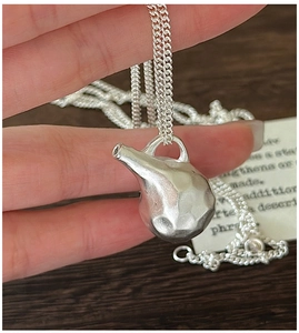 Macro shot of a matte silver-toned kettle pendant with hammer texture and double chain