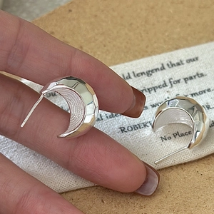 Hand holding textured S925 sterling silver crescent earrings with hammered finish effect