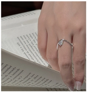 Macro shot of V-shaped silver ring with pear-cut stone worn on hand over a book