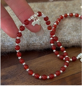 Détail d'un bracelet en perles d'agate rouge avec un pendentif mouton argenté vintage