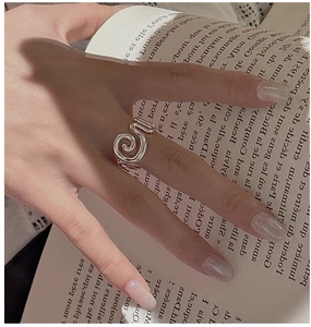Close-up of S925 sterling silver spiral ring on model hand with aesthetic book backdrop