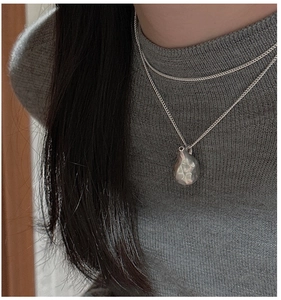 Detail view of irregular lava teardrop pendant with hammered texture on grey sweater