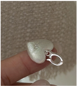Close-up of heart-shaped brushed silver pendant with a small zircon being held by hand