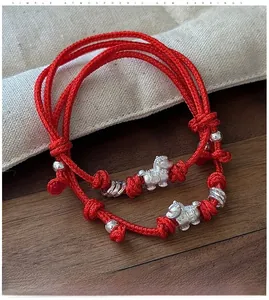 Detail of red braided string bracelet with silver horse charm on rustic burlap background