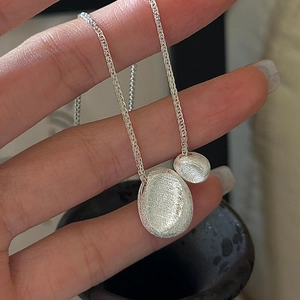 Hand holding S925 sterling silver double pebble pendant necklace with brushed texture