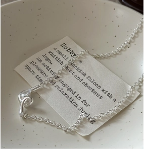 Macro shot of silver knot necklace featuring a teardrop zircon pendant and fine O-chain
