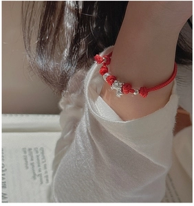 Detail of red braided lucky bracelet with silver elephant charm on a warm knit background