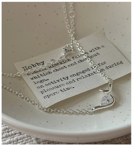 Close-up of S925 silver knot necklace with teardrop zircon pendant in a ceramic bowl