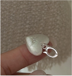 Macro detail of silver heart pendant with brushed texture and starburst setting on fingertip