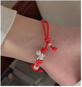 Detailed view of handmade red braided cord bracelet with silver ox charm and beads on wrist