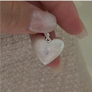 Close-up of heart-shaped S925 silver pendant with brushed texture and starburst gem