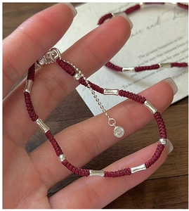 Detailed macro view of a red woven rope bracelet with silver bamboo-shaped metal accents