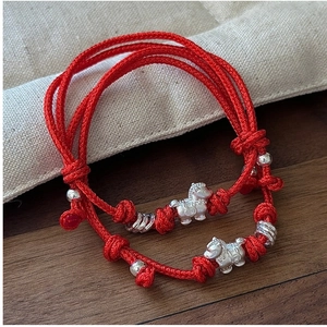 Macro detail of two handcrafted red woven bracelets with silver horse charms and beads
