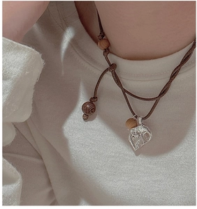 Close-up of a silver elephant pendant on a brown woven cord worn over a white sweater