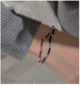 Detail of woven rope bracelets in red and black with silver metal tubes on wrist