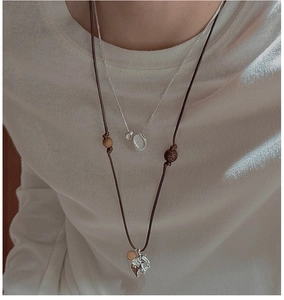 Detail of layered S925 silver necklace with heart pendant and wooden beads on white T-shirt