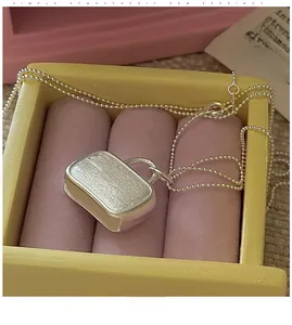 Close-up of S925 silver handbag pendant with brushed texture on a pink velvet display