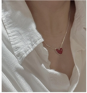 Dettaglio della collana con ciondolo a cuore rosso e bordo dorato su modella elegante
