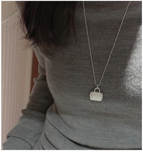 Macro view of textured silver bag pendant on a minimalist necklace with fine bead chain