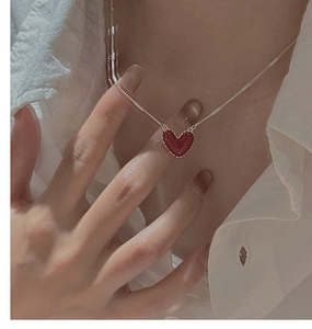 Dettaglio del ciondolo a cuore rosso smaltato su catena d'argento indossato su camicia bianca