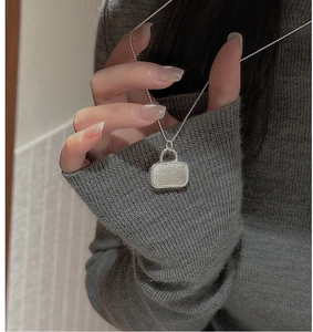 Detail of S925 sterling silver handbag pendant necklace with brushed texture on grey sweater