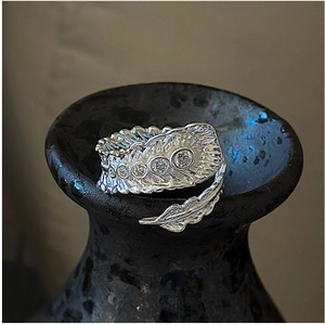 Macro shot of silver feather ring with five sparkling zircons on aged ceramic texture