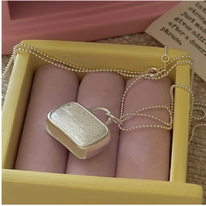 Macro detail of silver purse pendant with brushed texture on a delicate bead chain