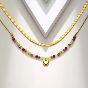 Detail of layered gold snake chain and colorful beaded necklace with a heart pendant