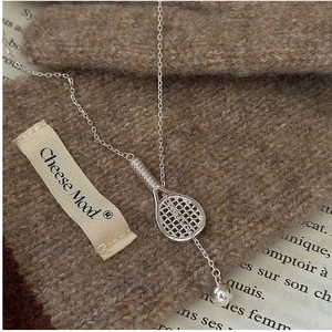 Close-up of S925 silver tennis racket pendant and ball necklace on a knit background