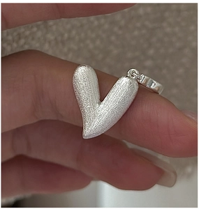Vue macro d'un pendentif cœur en argent avec finition mate texturée entre les doigts