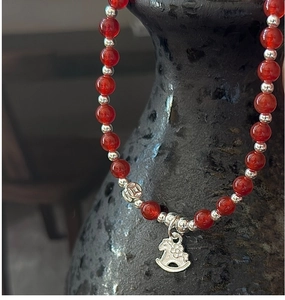 Détail des perles d'agate rouge et du charm cheval à bascule sur bracelet élastique