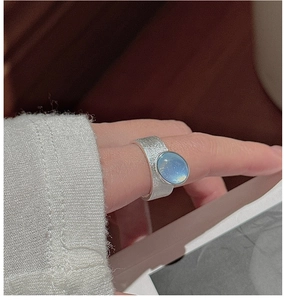Detail of matte wide silver band ring featuring a large oval blue gemstone on a finger