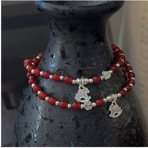 Détail de bracelets en agate rouge avec pendentif cheval argenté sur vase en céramique