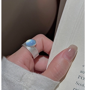 Close-up of wide brushed silver ring with oval blue moonstone on vintage book