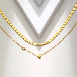 Detailed close-up of layered gold herringbone chain with a polished heart pendant and crystal