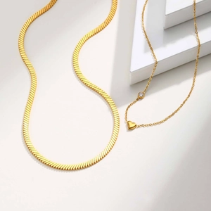 Close-up of layered gold herringbone snake chain and heart pendant with round diamond detail