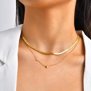 Detail of layered gold herringbone and heart pendant necklace worn on a model
