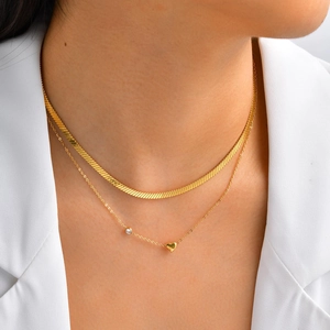 Close-up of layered gold snake chain necklace with heart pendant and zircon on a model