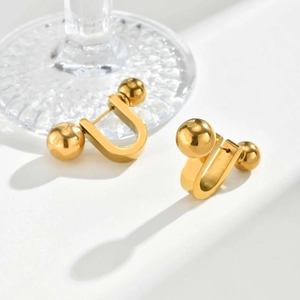 Detail von goldenen U-förmigen Kugelohrringen mit Hochglanzfinish auf Glasdekor