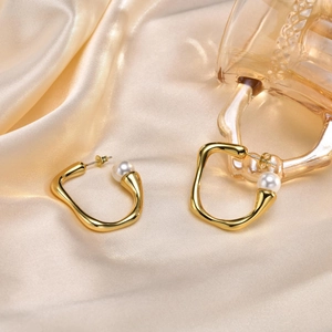 Detailed shot of irregular gold wave earrings with white pearls on champagne silk fabric