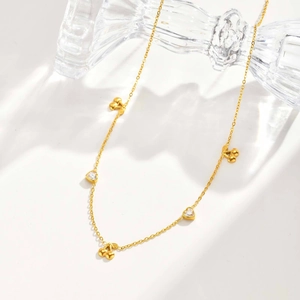 Detail view of golden necklace with heart crystals and cherry charms on white background