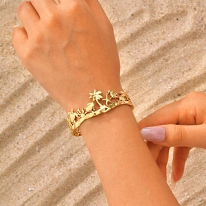 Détail du bracelet tropical doré avec hippocampe et palmier sur fond de sable