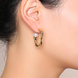 Close-up of golden irregular U-shaped earrings with pearls on model's ear